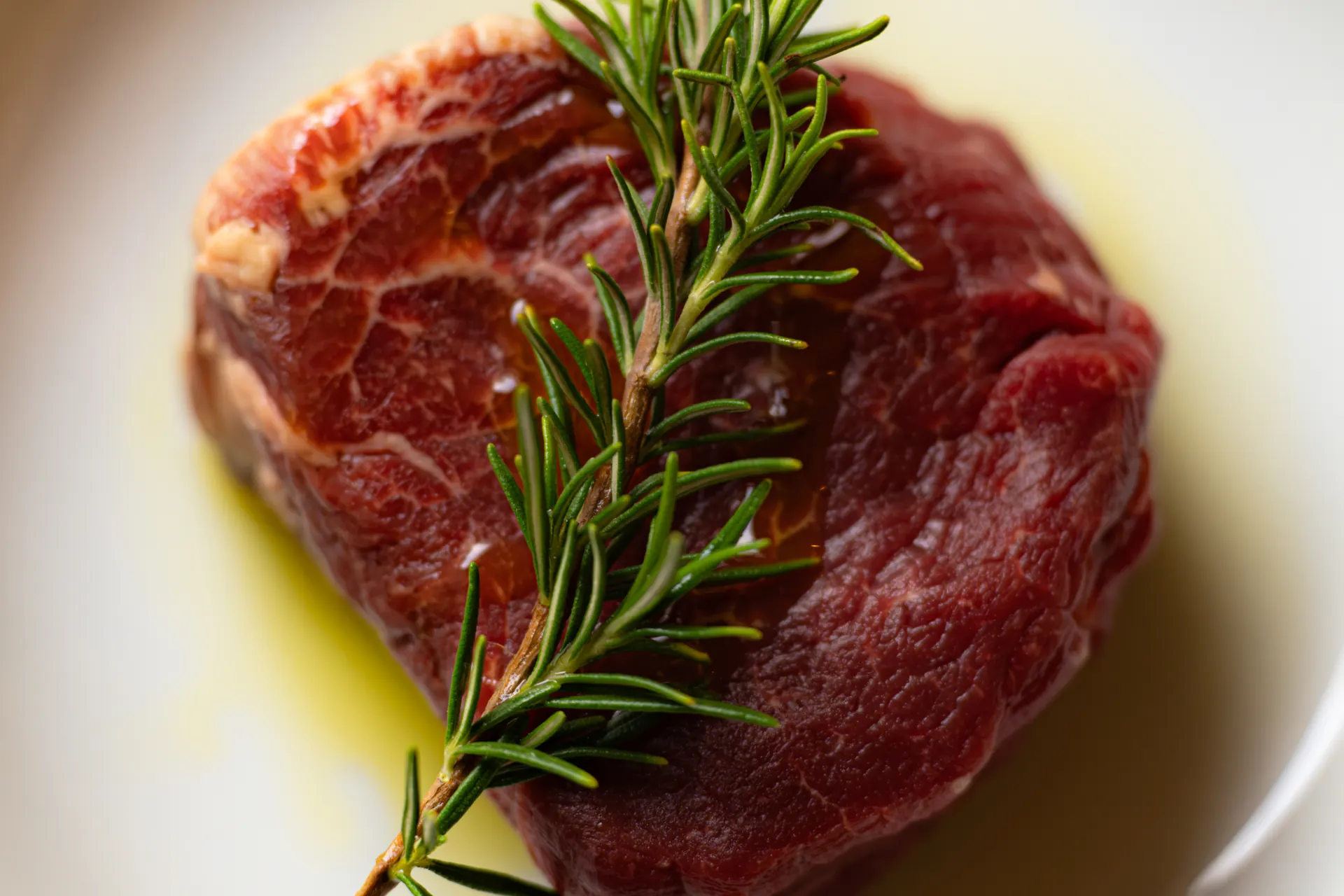 Beef fillet with a sprig of rosemary in olive oil, ready for the grill