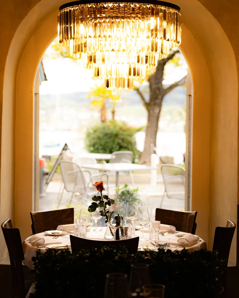LAGO dining room: a crystal chandelier and a set round table, the arched door open onto the terrace and Lake Zurich