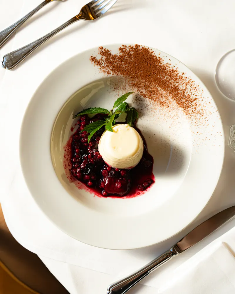 Panna cotta with warm berries and mint, a dusting of cocoa on the plate