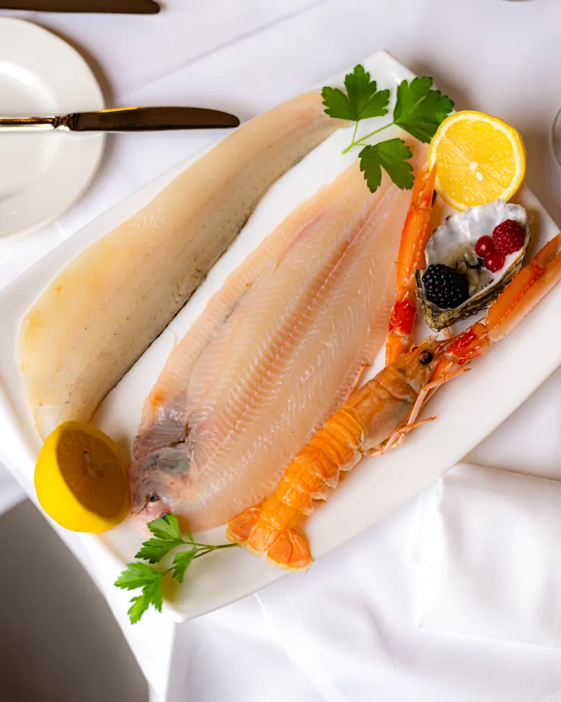 Sole fillets with a langoustine, lemon and parsley on a white platter