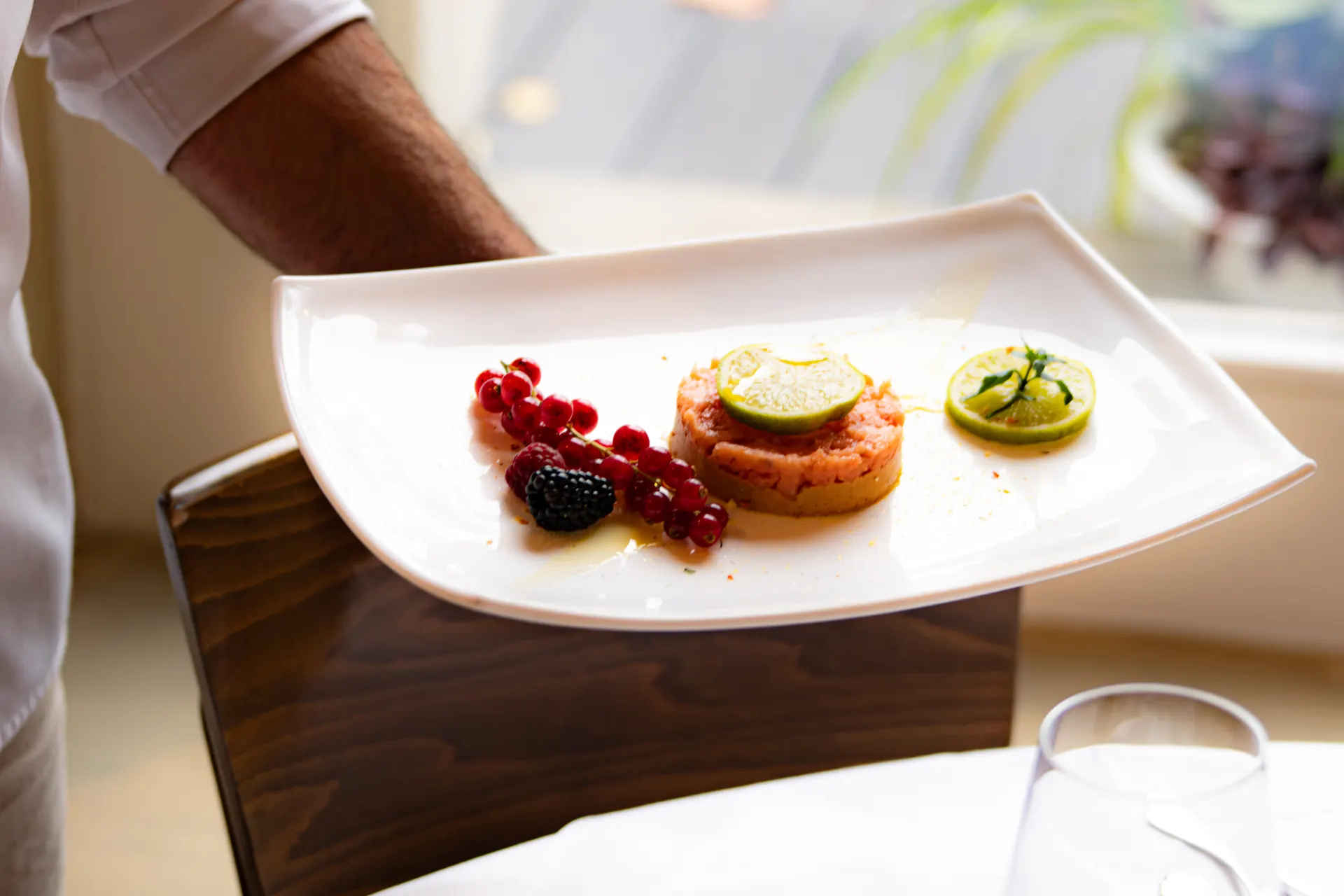 A waiter carries salmon tartare with lime and fresh berries to a table by the window