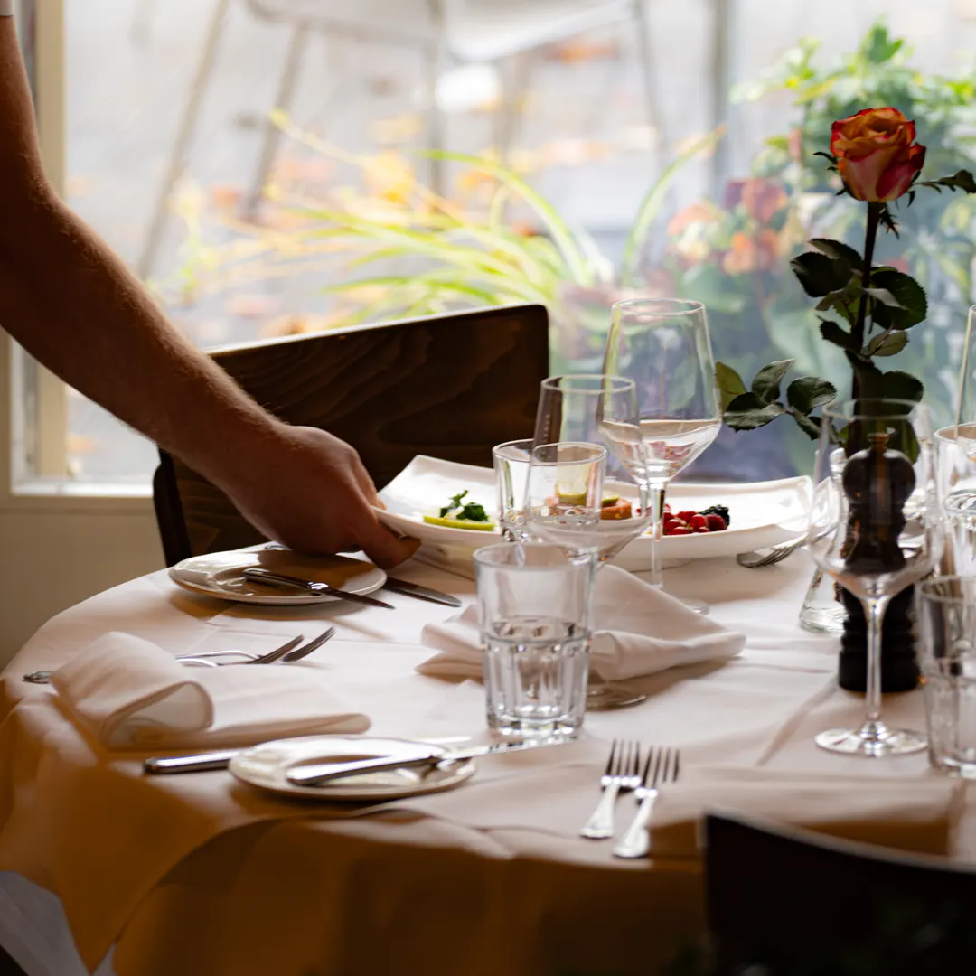 A waiter serves a starter at a set table by the window onto the terrace